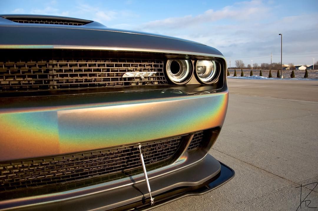 Close-up of a black car front with a rainbow-tinted bumper on a sunny waterfront drive
