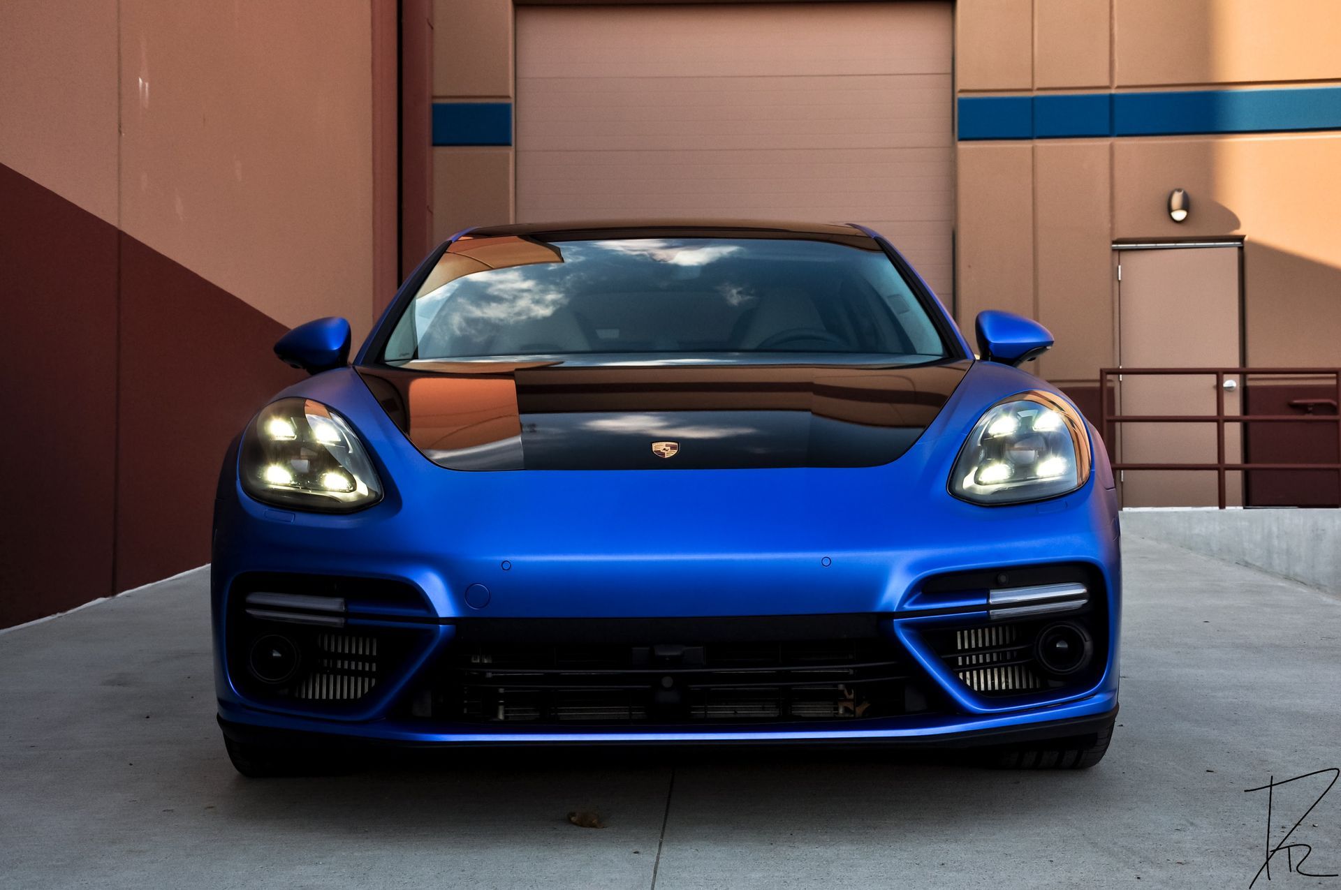 Blue sports car parked in front of a modern building, shown from the front.