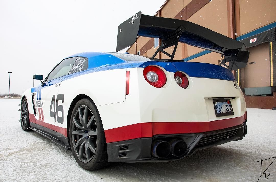 Race car rear view, white with blue and red accents, parked with a large rear wing in a pit area