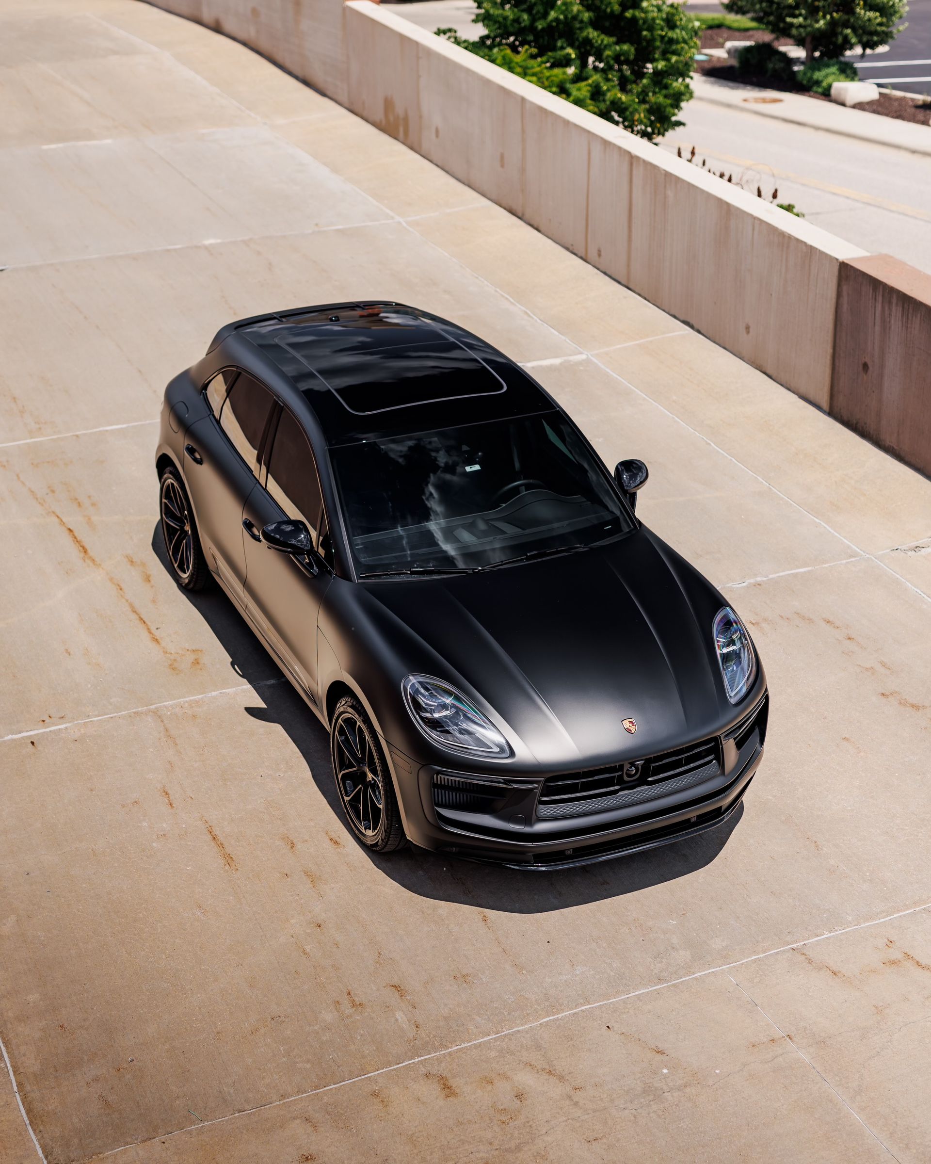 Black SUV on a sloped concrete driveway beside a tan retaining wall, viewed from above.