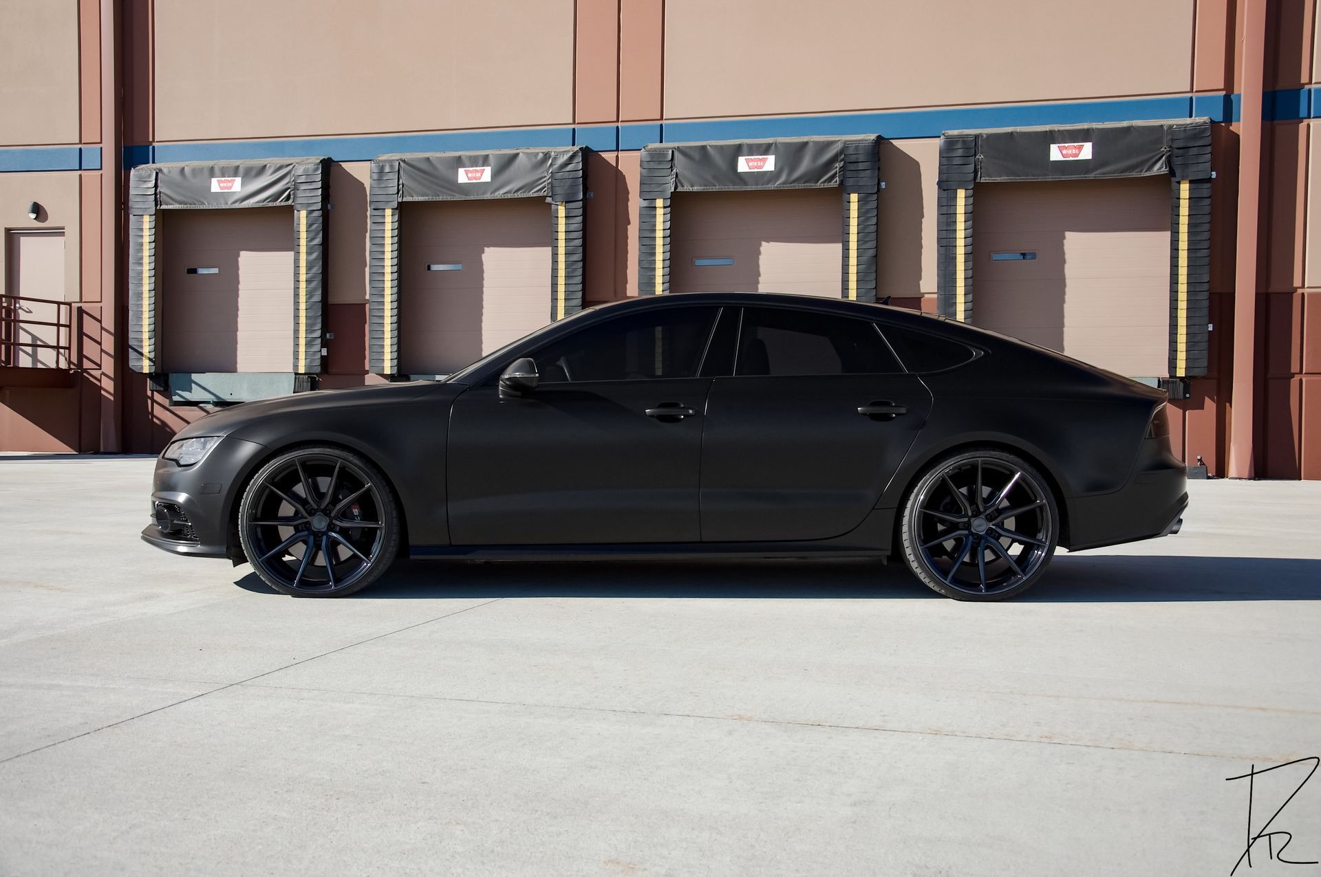 Matte black sports sedan parked in front of a building with garage doors
