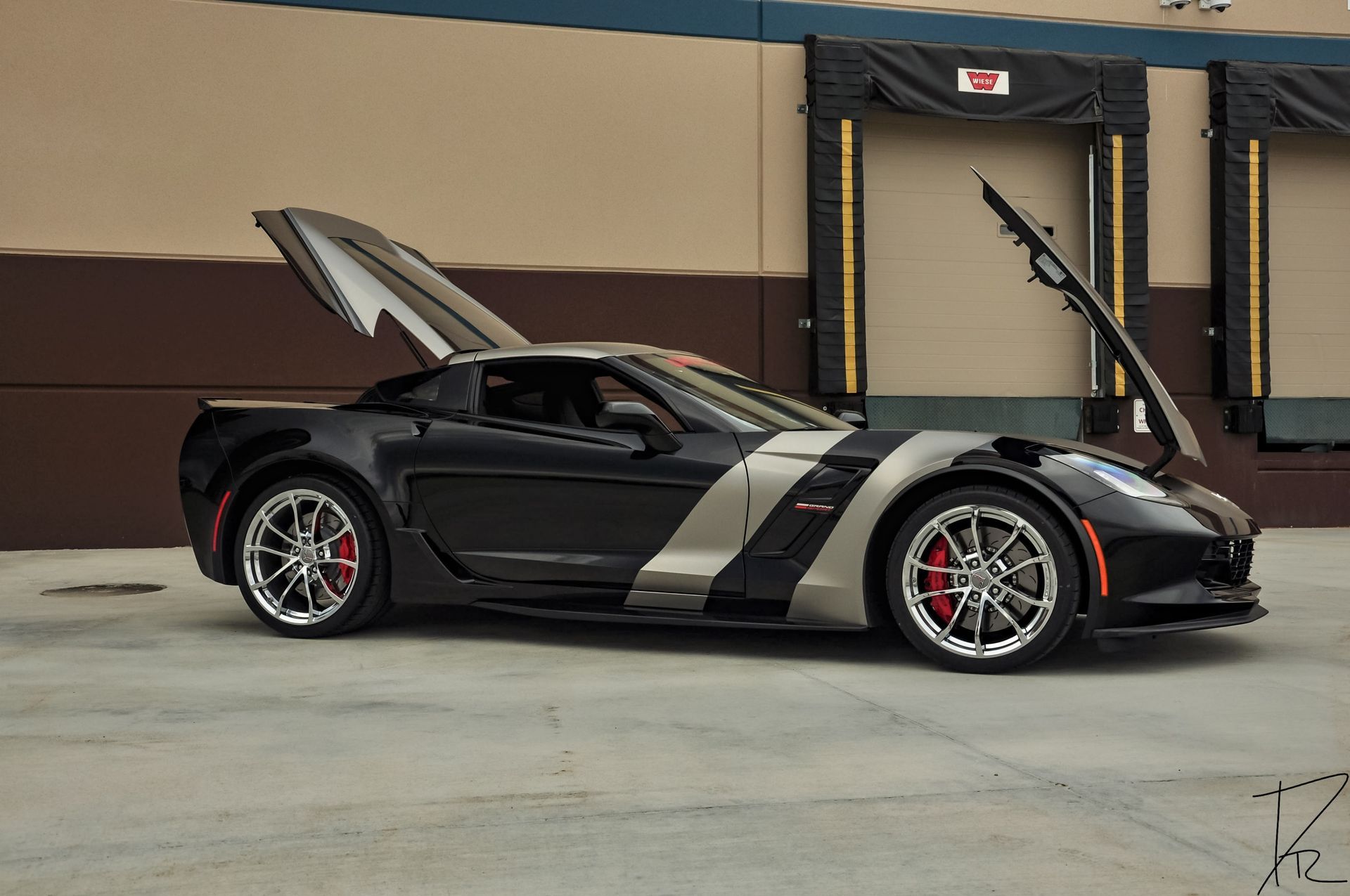 Black sports car with silver racing stripes and open scissor door parked in a garage