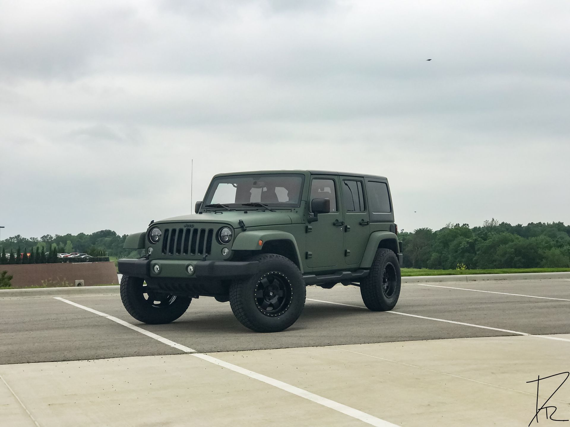 Green Jeep Wrangler on an empty rooftop parking lot under a cloudy sky.