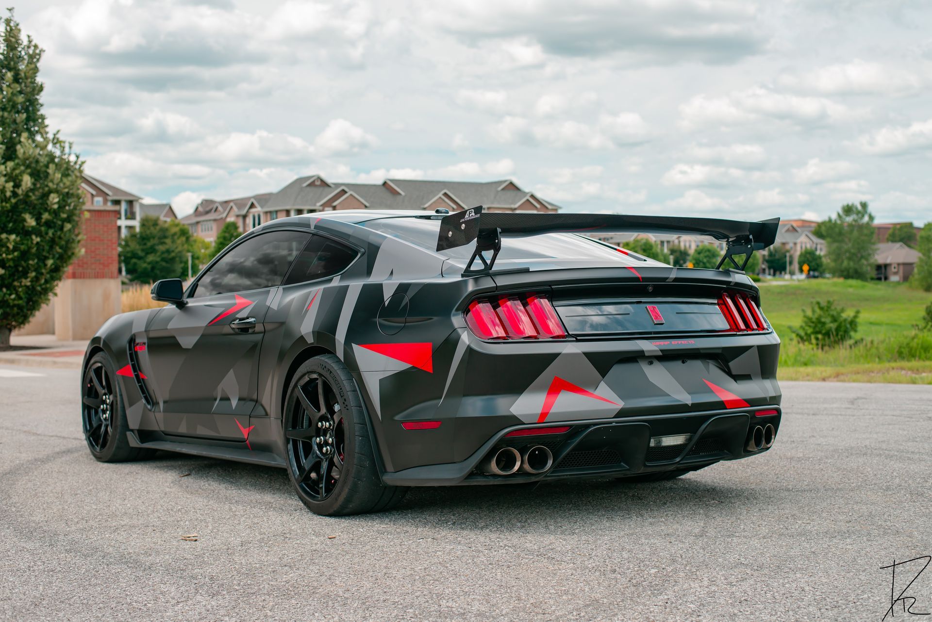 Black sports car with red accents parked on a gravel road in a suburban neighborhood