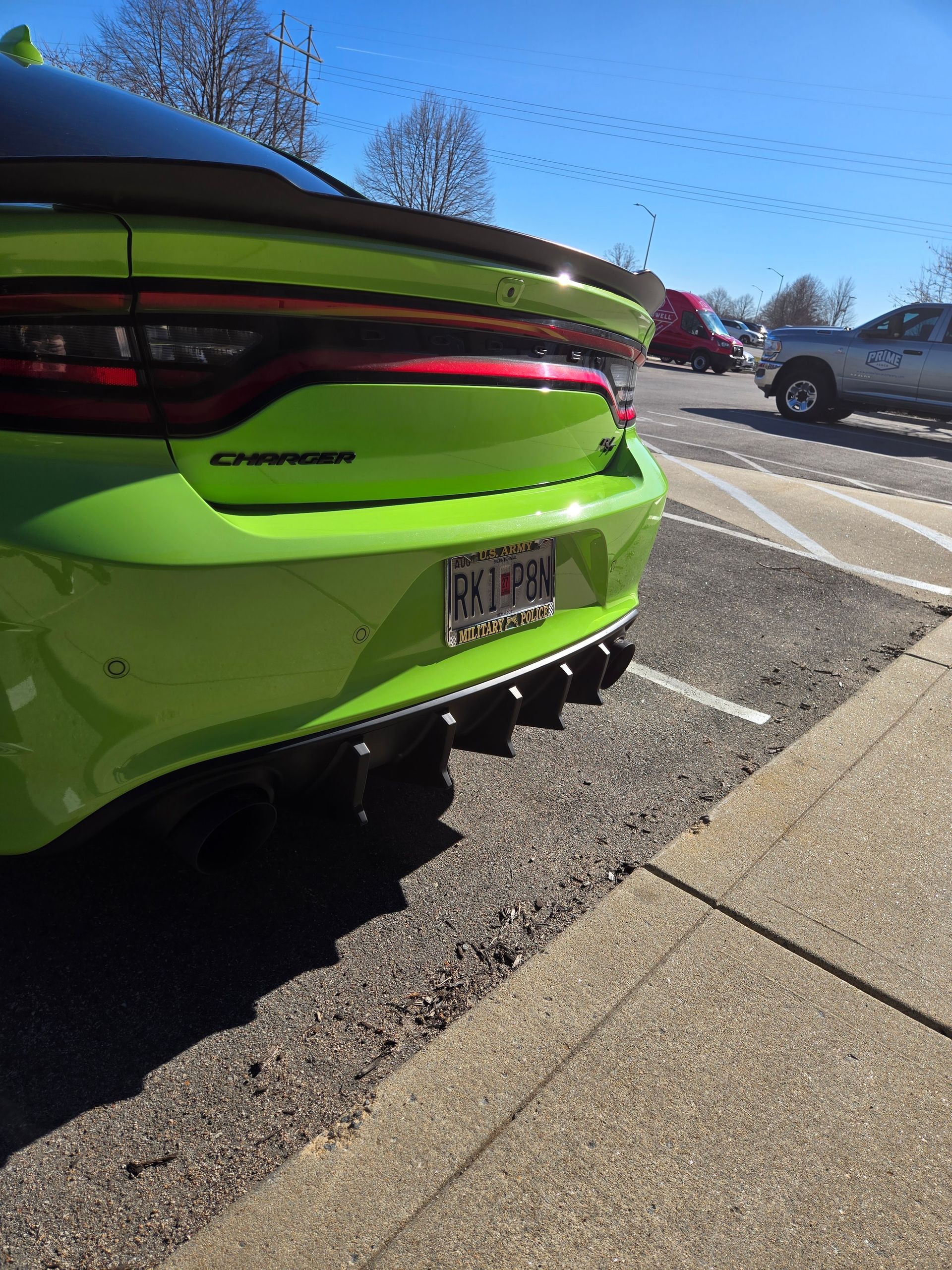 Rear view of a lime green Dodge Charger parked by a sidewalk on a sunny street.