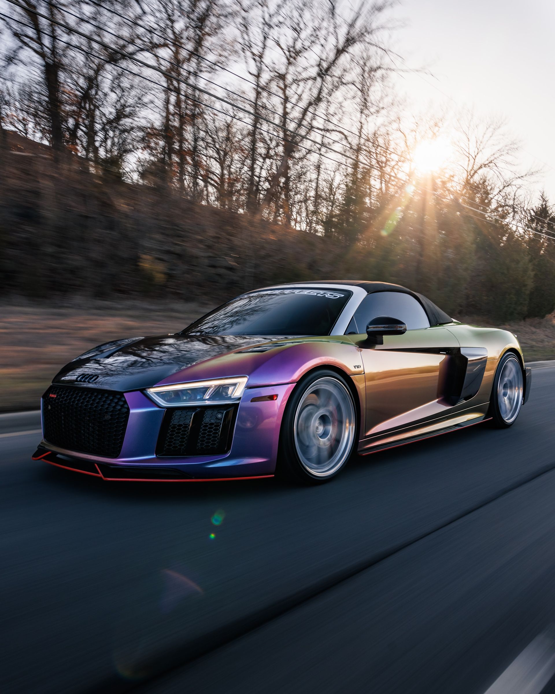 Purple sports car driving on a road at sunset, with trees in the background