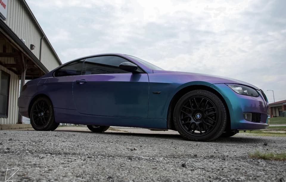 Purple-to-blue gradient sports car parked beside a building on a gravel lot