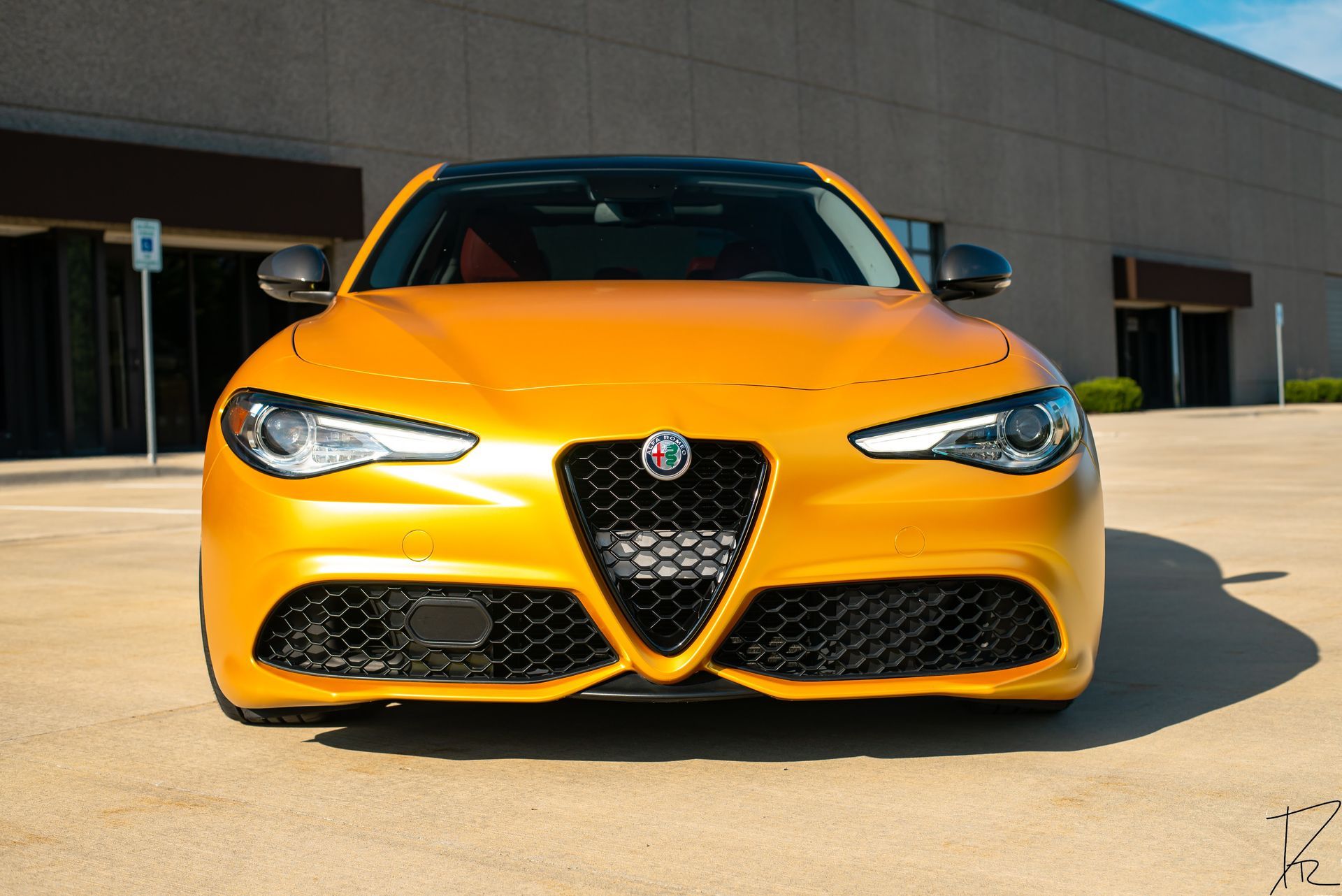 Front view of a yellow Alfa Romeo sports car parked outdoors in front of a building.