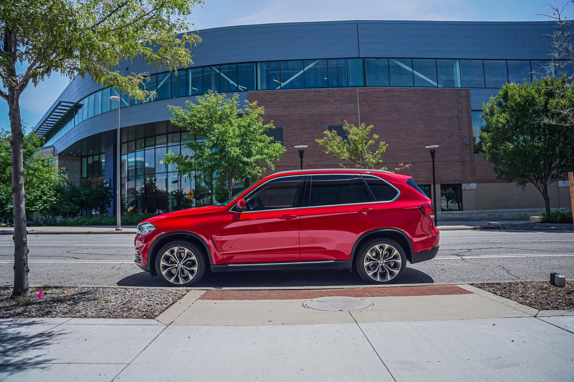 Red SUV parked on a city street in front of a modern glass-and-brick building.