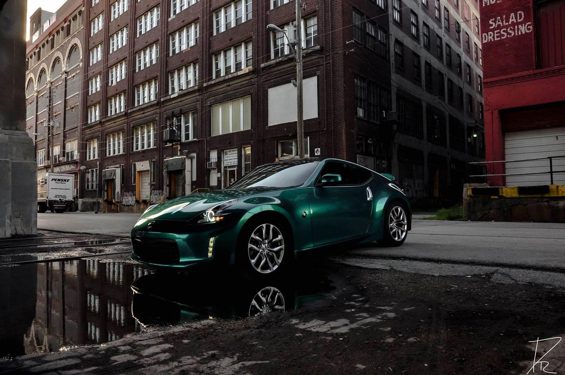 Green sports car parked on a wet city street beside brick buildings and a puddle reflection