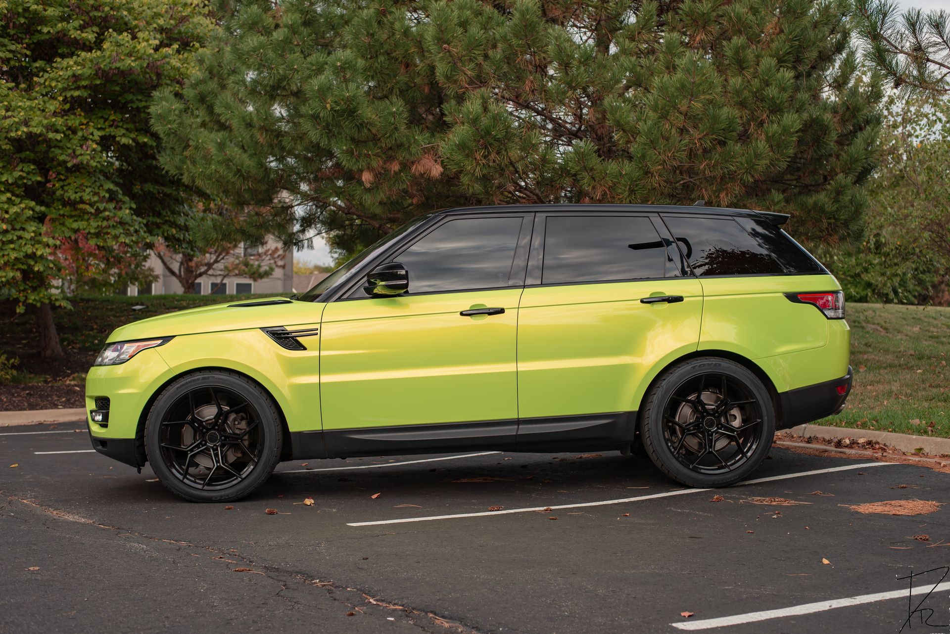 Bright lime-green SUV with black roof parked on a street beside trees.
