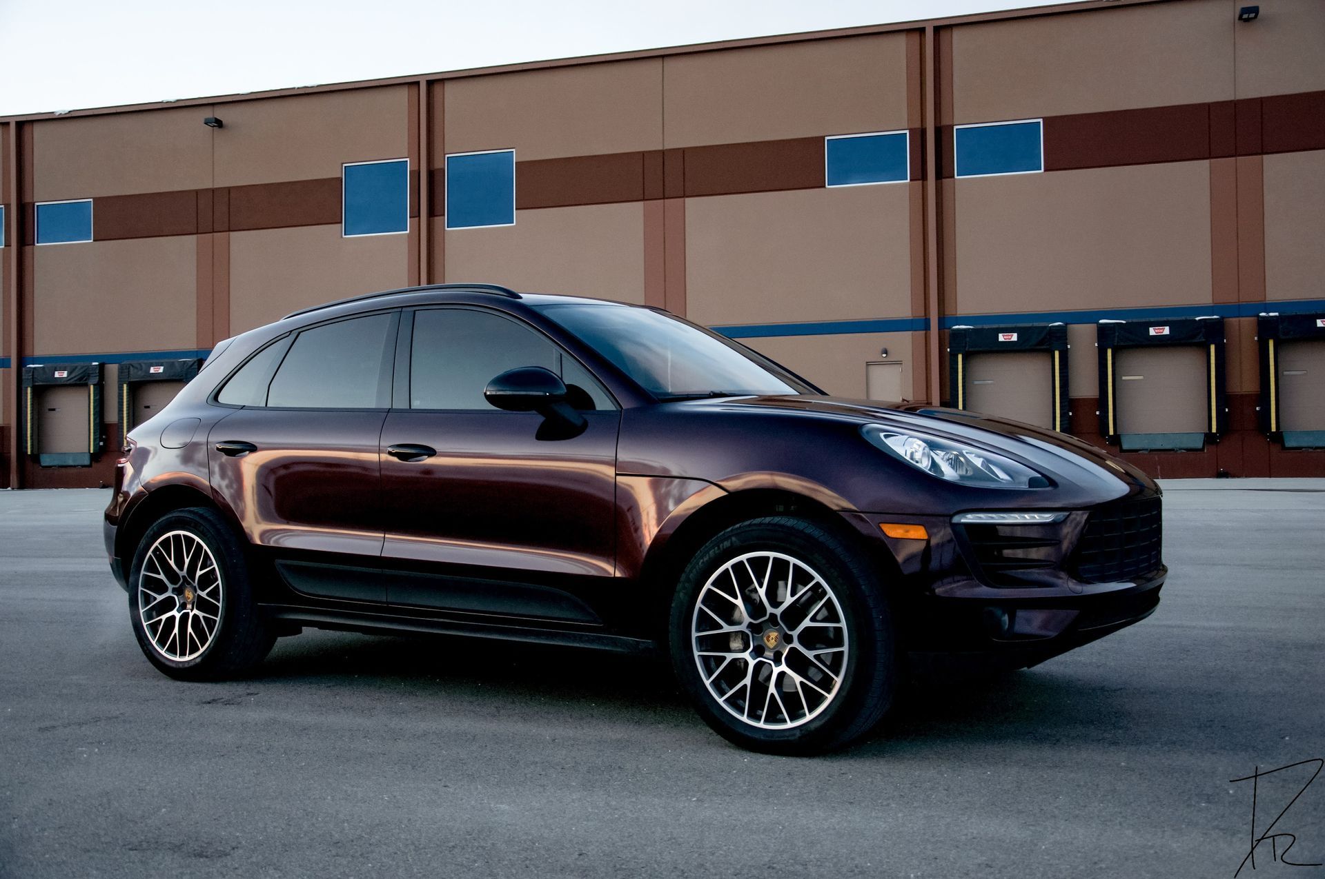 Dark maroon SUV parked in front of a beige industrial building on a paved lot