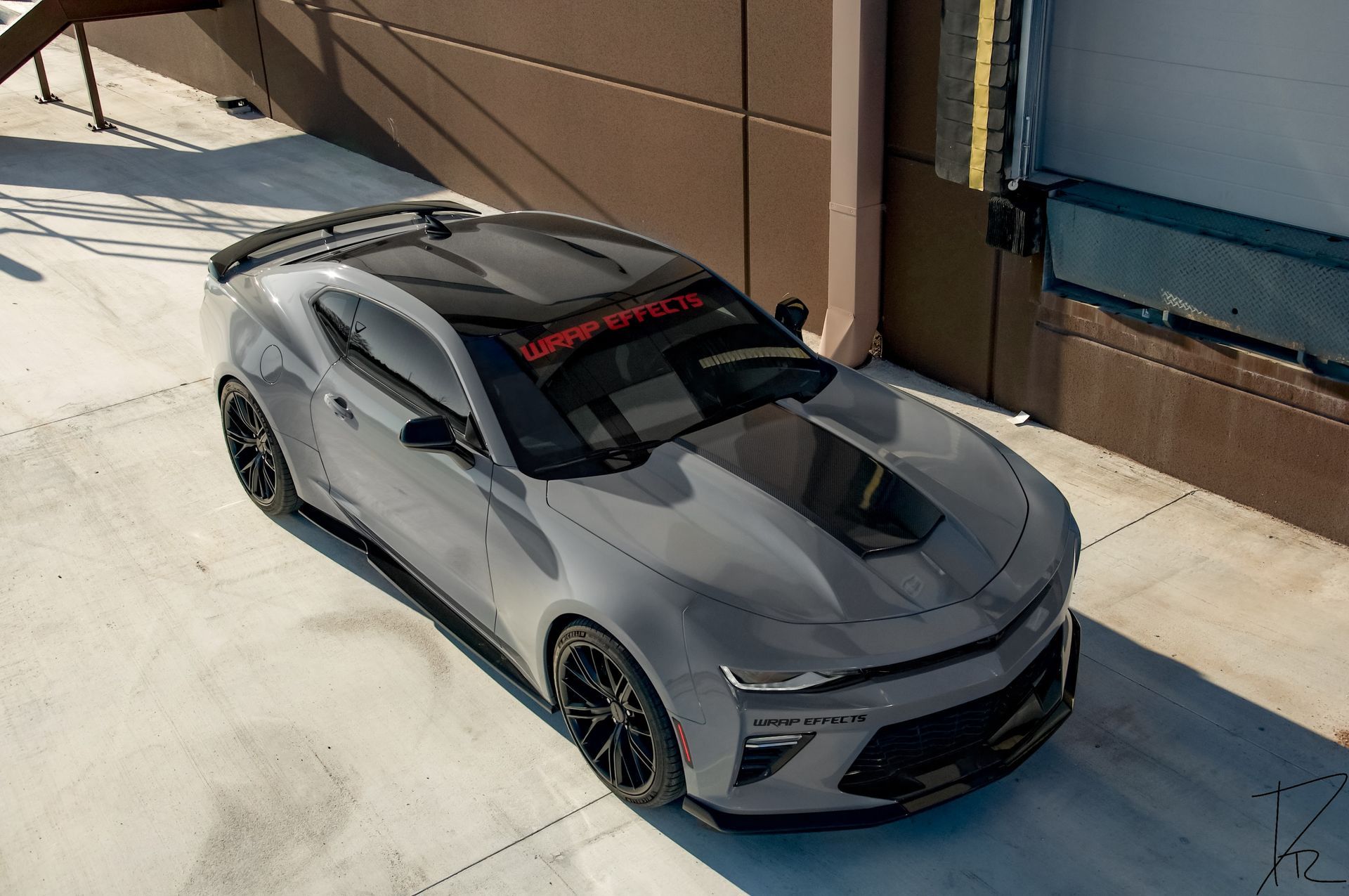 Gray sports car parked beside a building, viewed from above in bright sunlight