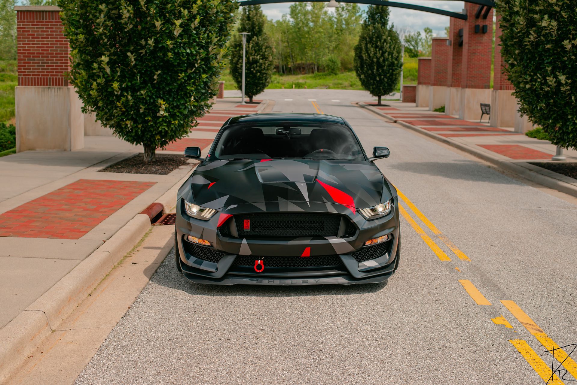 Black sports car with red accents parked on a tree-lined street in front of brick buildings.