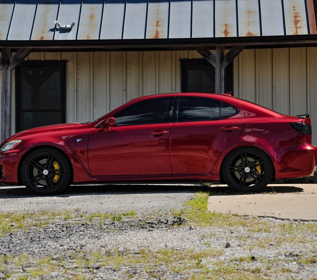 Red sports sedan parked beside a weathered metal building on a gravel lot.