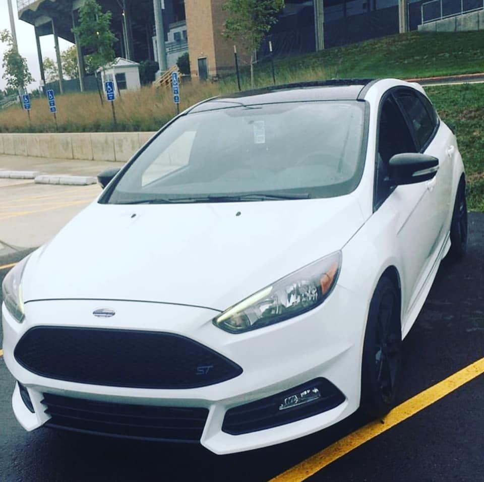 White hatchback car parked in a lot, angled front view on a wet street.