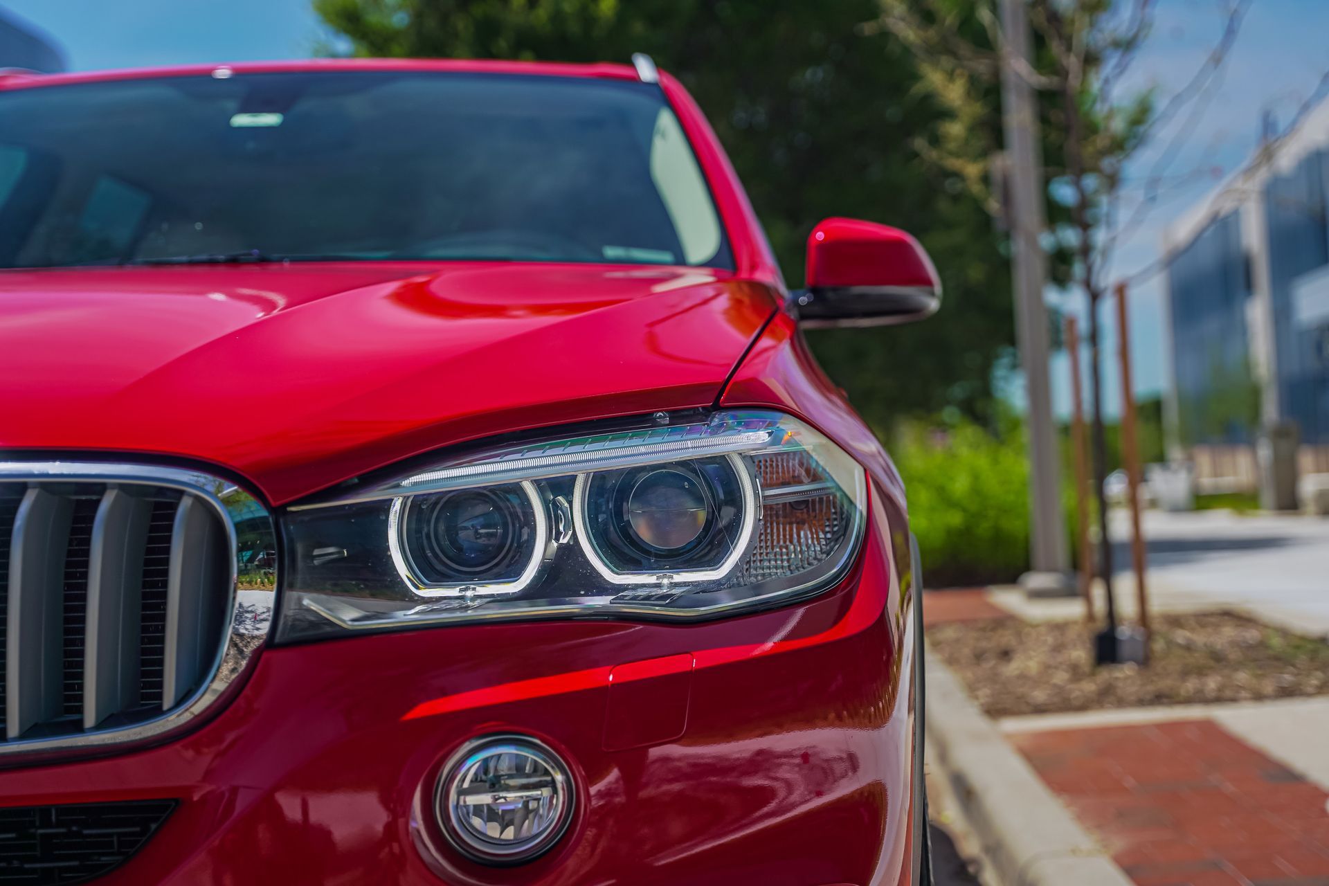 Close-up of a red BMW front headlight and grille parked outdoors on a street