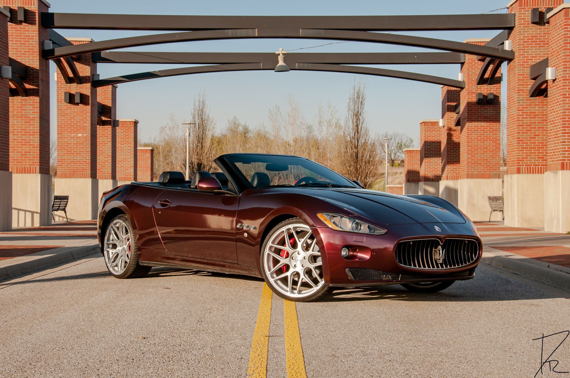Maroon convertible sports car parked on a road beneath brick arches