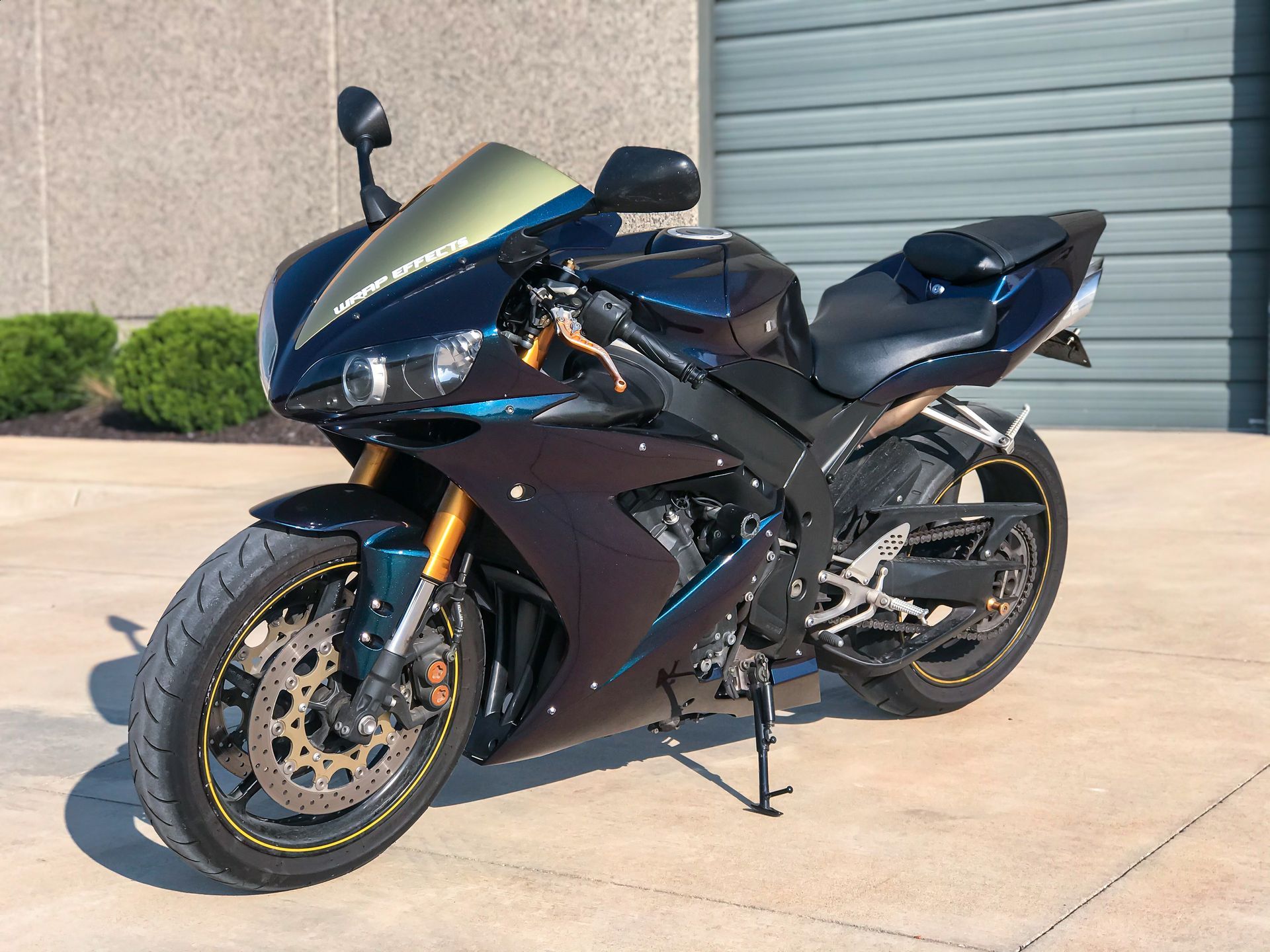 Black sport motorcycle parked on a concrete driveway in front of a gray garage door.