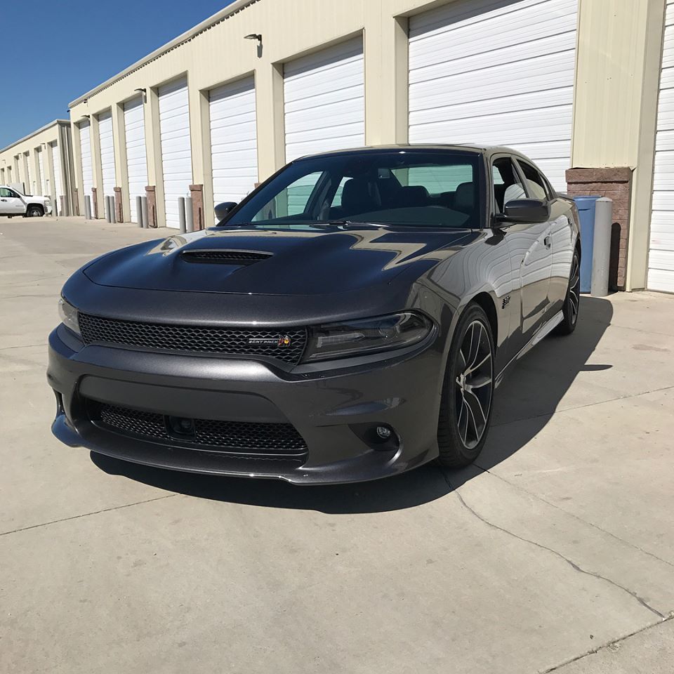 Black Dodge Charger parked outside industrial garage doors in bright sunlight