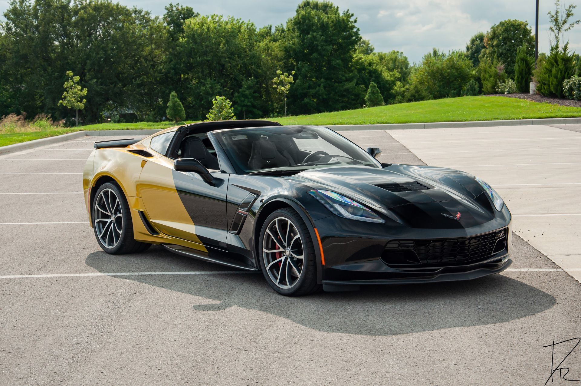 Black and gold convertible sports car parked on an empty lot with trees in the background