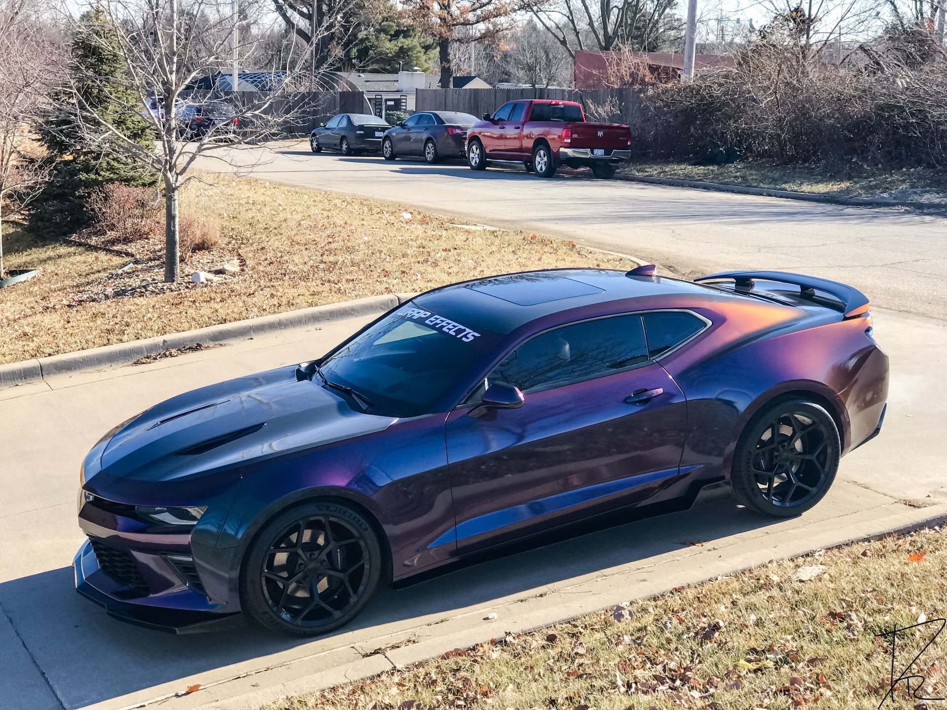 Purple sports car parked on a suburban street beside a sidewalk and trees