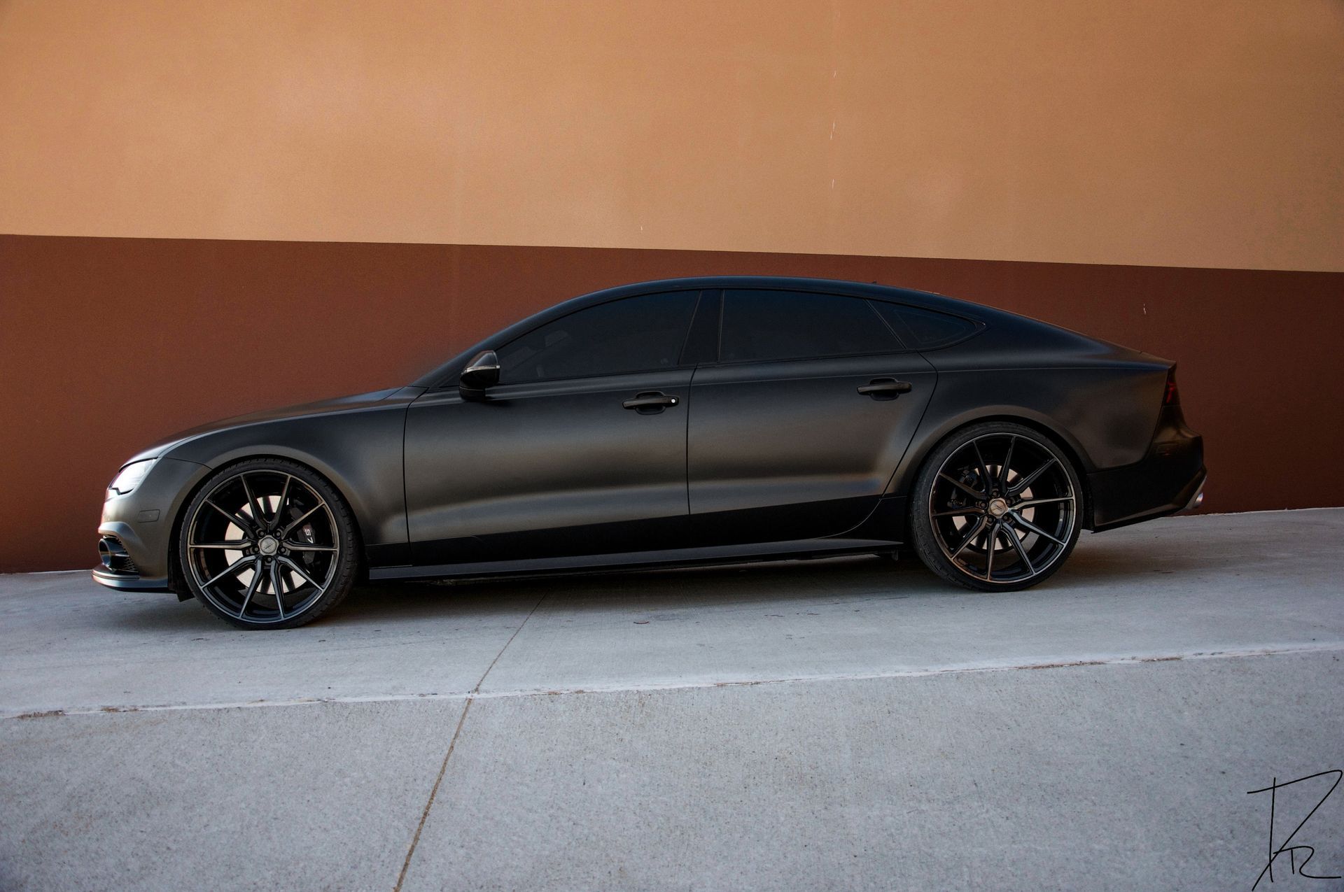 Black sports coupe parked on a street against a tan wall