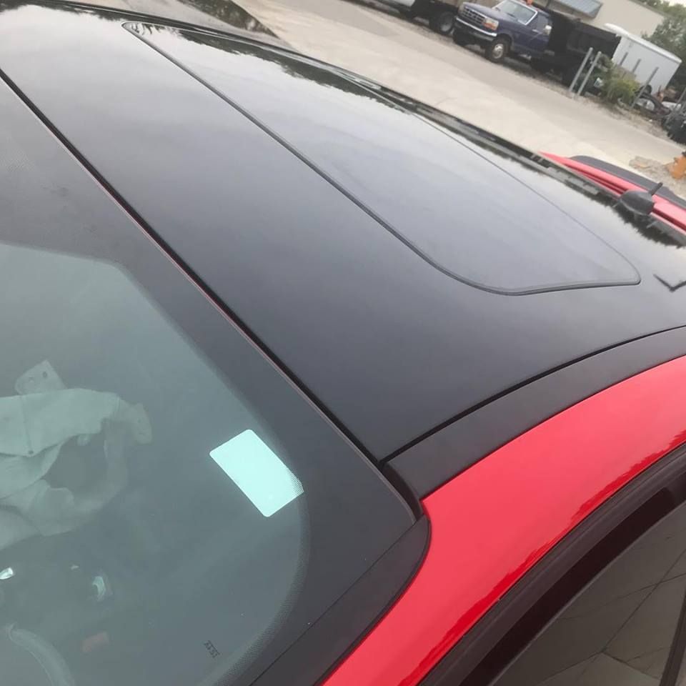 Close-up of a black car roof and windshield next to a red car in a parking lot