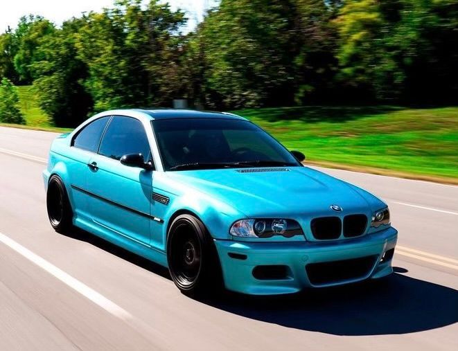 Bright blue sports coupe driving on a sunny road with blurred green trees in the background