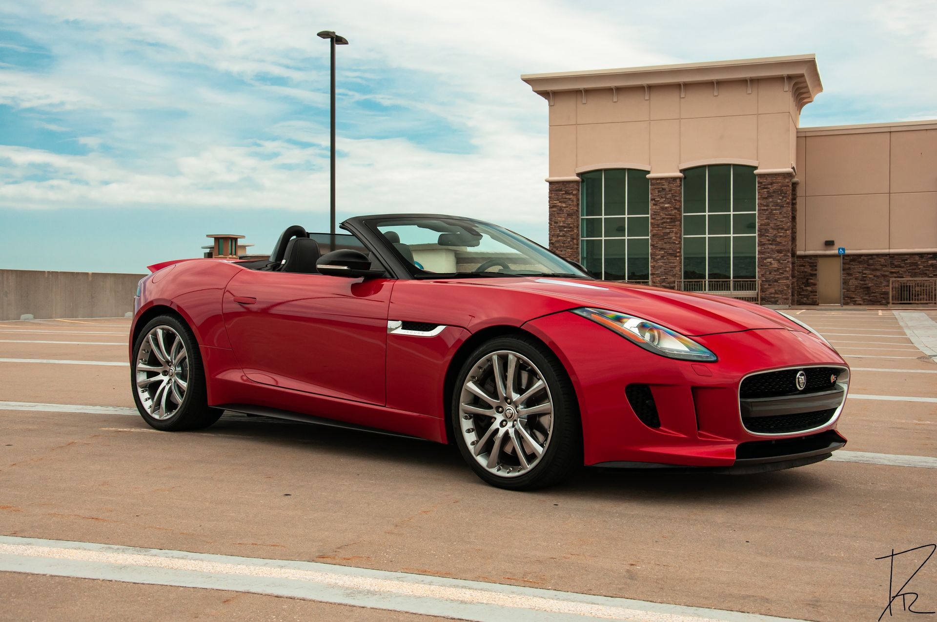 Red convertible sports car parked on a rooftop lot with a building in the background.