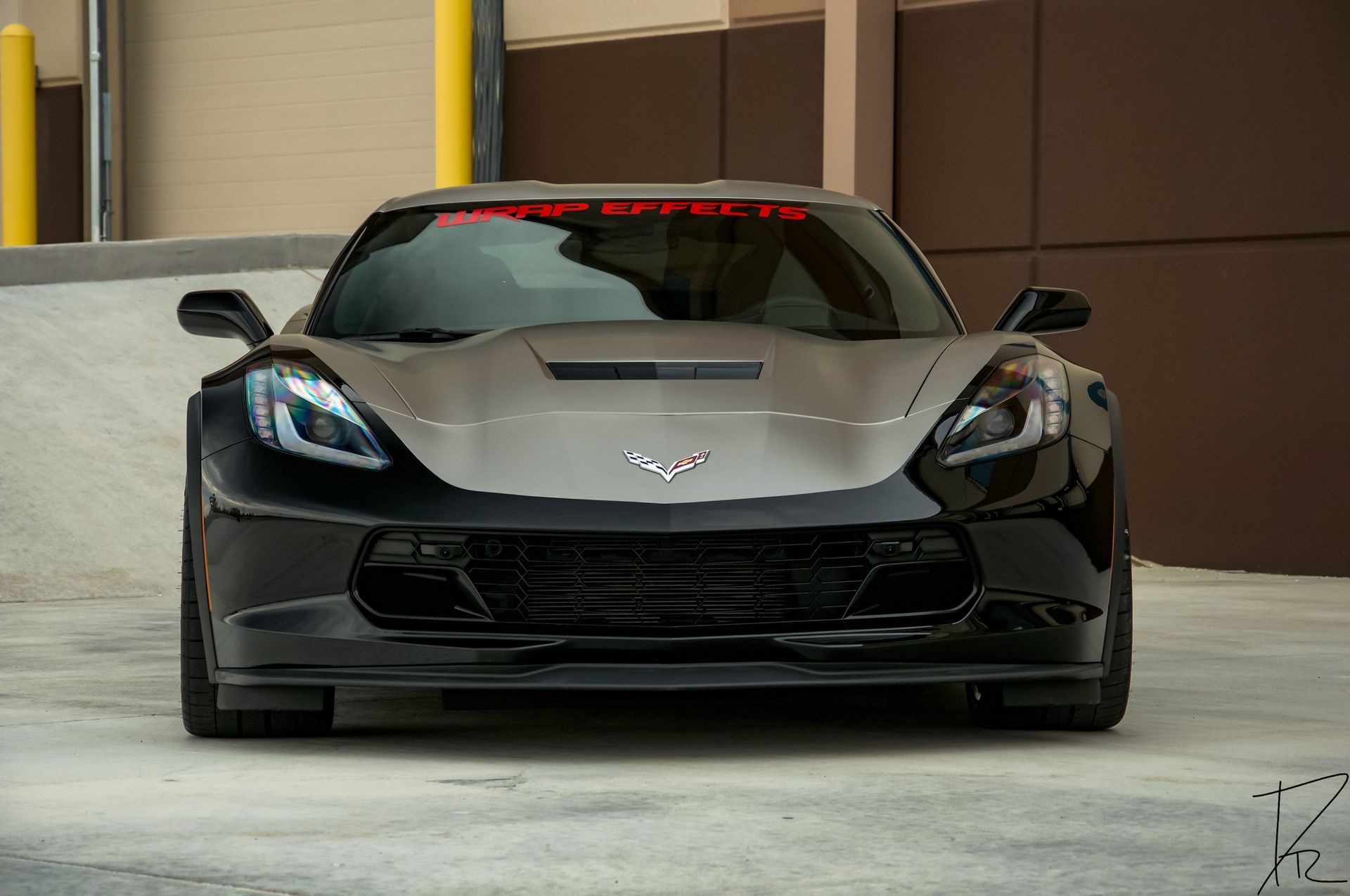 Front view of a black sports car with blue headlights parked indoors on a concrete floor