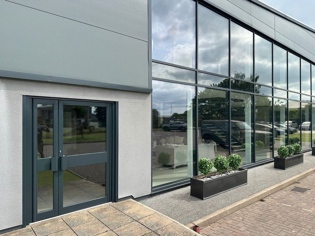 The same aluminium entrance doors and handles after spraying, matching the dark grey curtain walling alongside