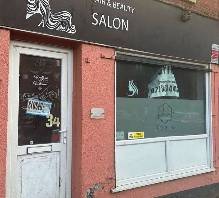 Shop front before respraying, with faded pink rendered walls and the previous salon's black sign board