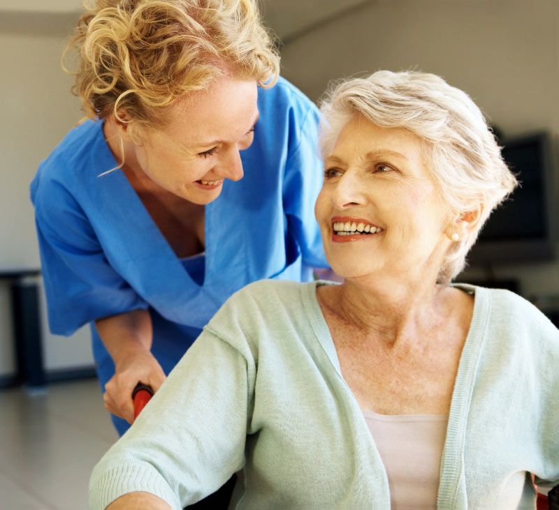 Friendly caregiver assisting a smiling senior woman during an in-home care assessment for personalized elderly care services.