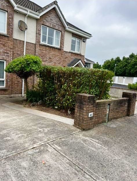 Brick facade house with a small tree, a trimmed hedge, and a brick wall. Gray overcast sky.
