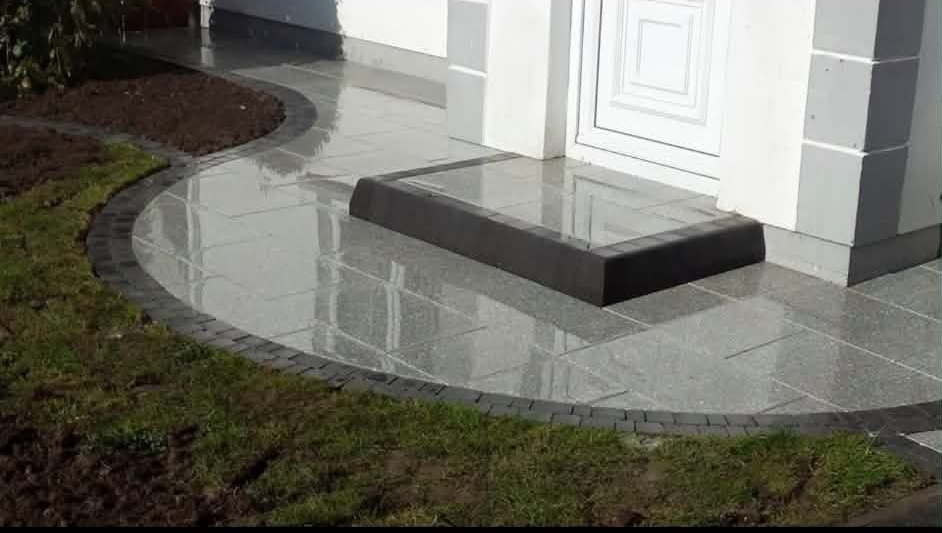 Raised wooden garden bed with tiled patio and steps. Green grass borders.