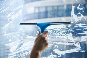 Hand using a blue squeegee to clean a glass window with soap streaks