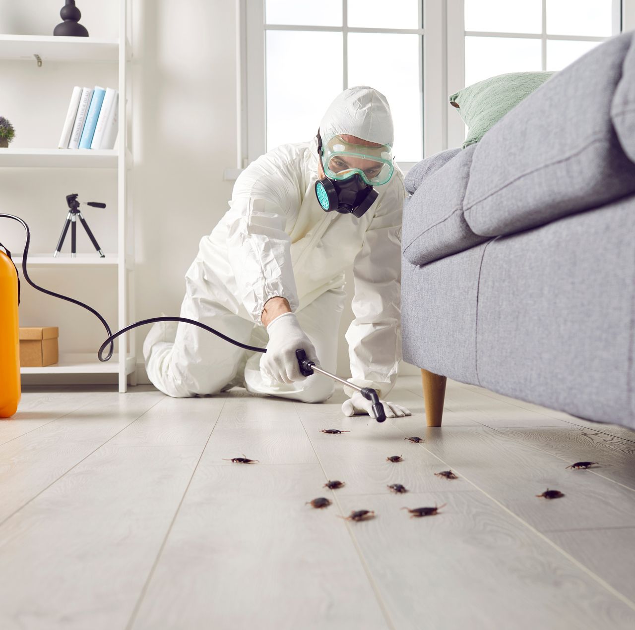 A man in a protective suit is kneeling on the floor in a living room.