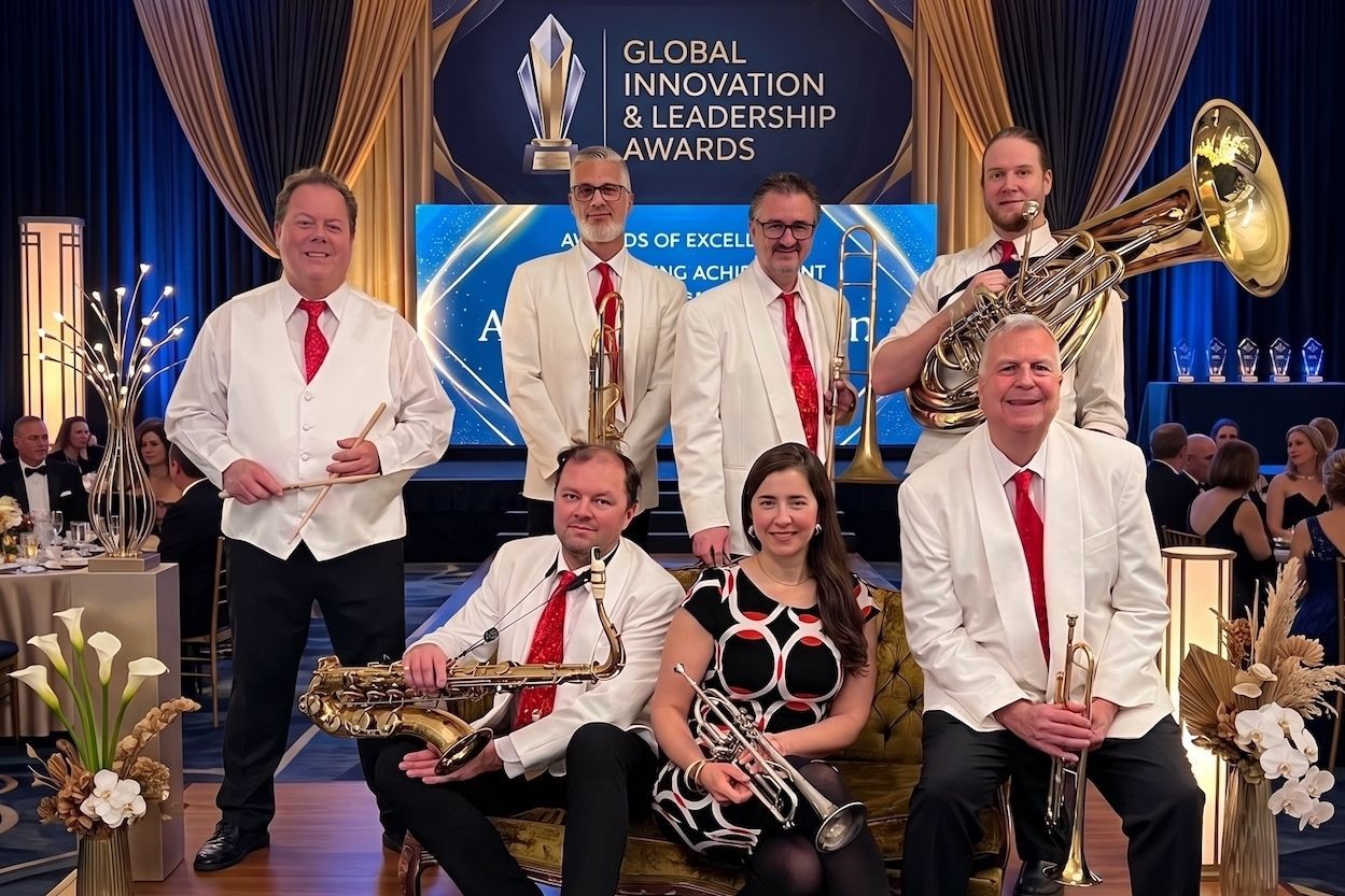Band in white jackets posing onstage at a Global Christian Music Awards event with blue lighting and trophies