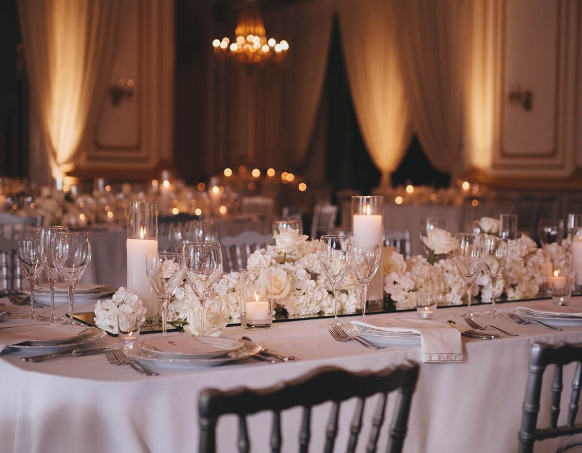 Elegant banquet table with white floral centerpieces and candlelight in a softly lit ballroom