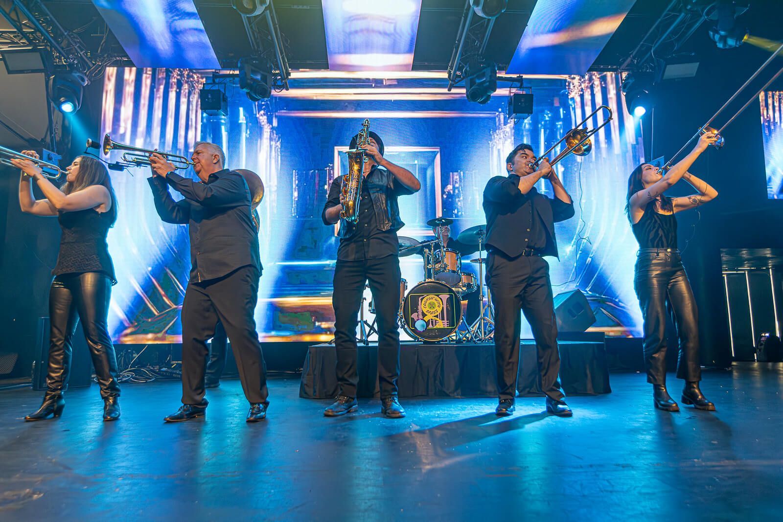 Five musicians performing on a blue-lit stage with bright beams and instruments.