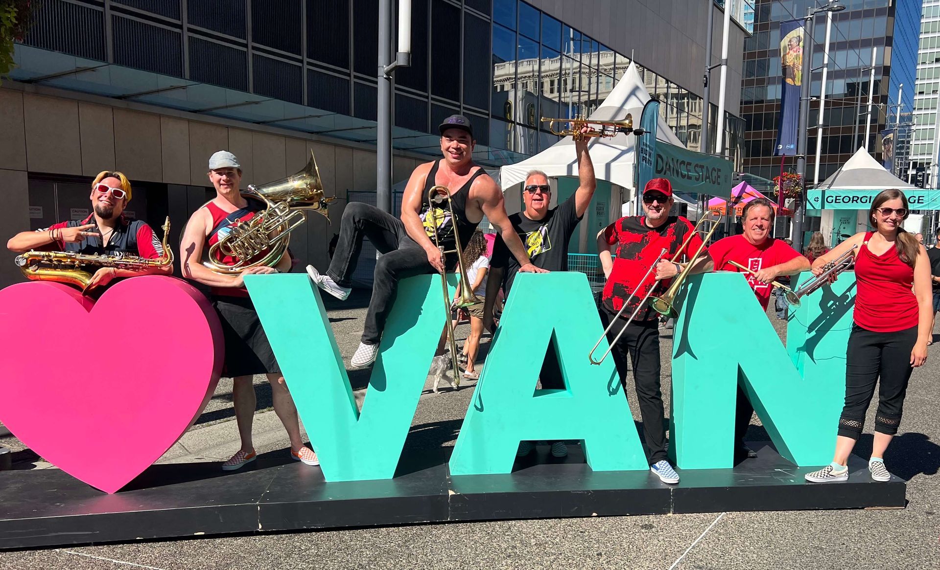 People posing behind giant pink heart and turquoise “I <3 VAN” sign at a street event