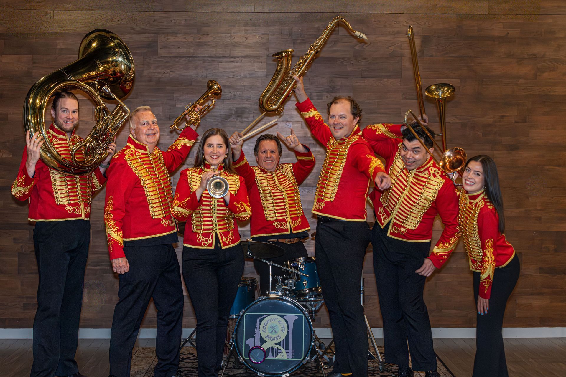 Red-jacketed brass band performing on stage with trumpets, trombone, and tuba in front of drums