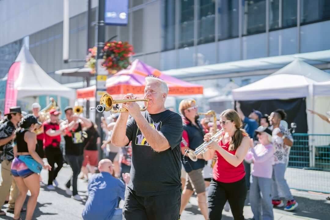 Street musicians performing in a sunny outdoor market with onlookers and colorful tents