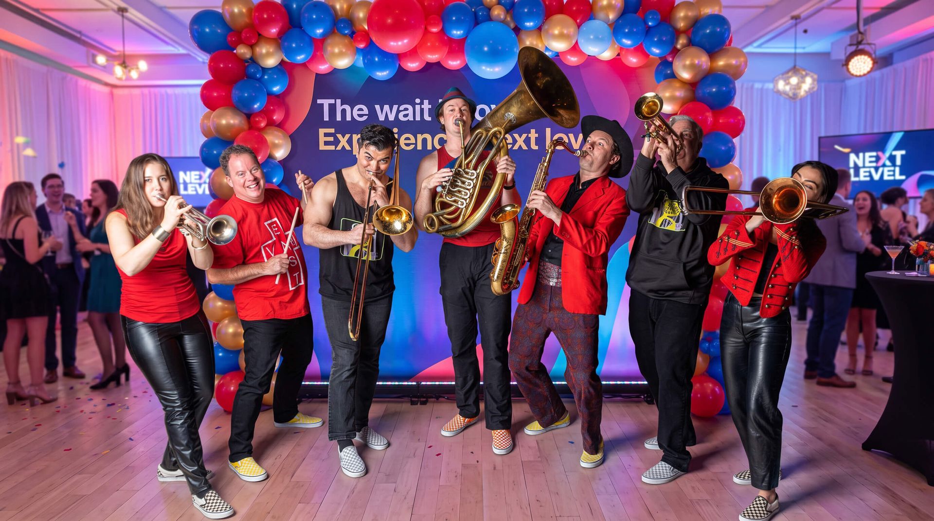 Dancers in red and black perform on a stage under red, white, and blue balloons at a festive event