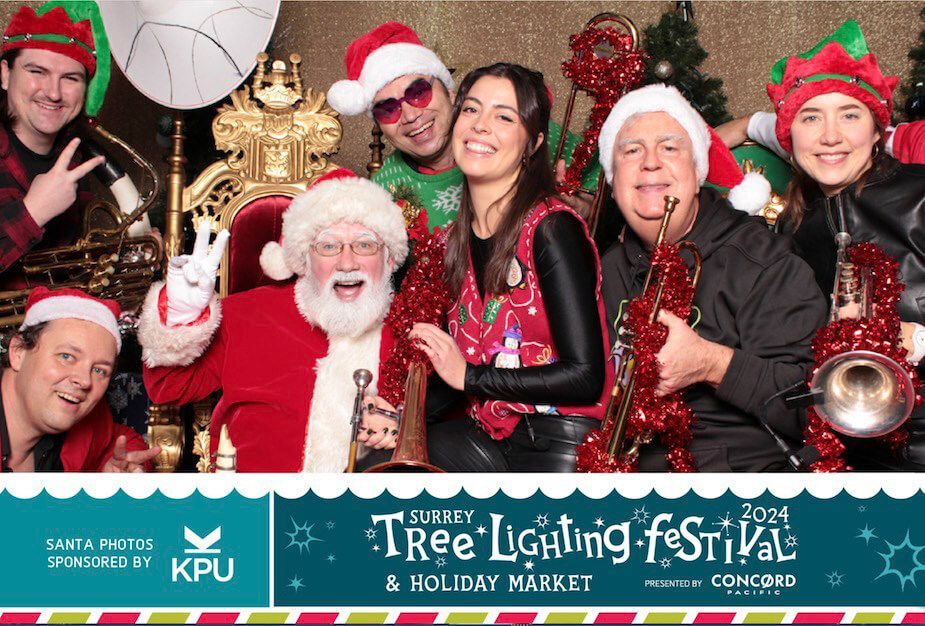 Holiday group photo with Santa, festive hats, and a tree lighting festival banner