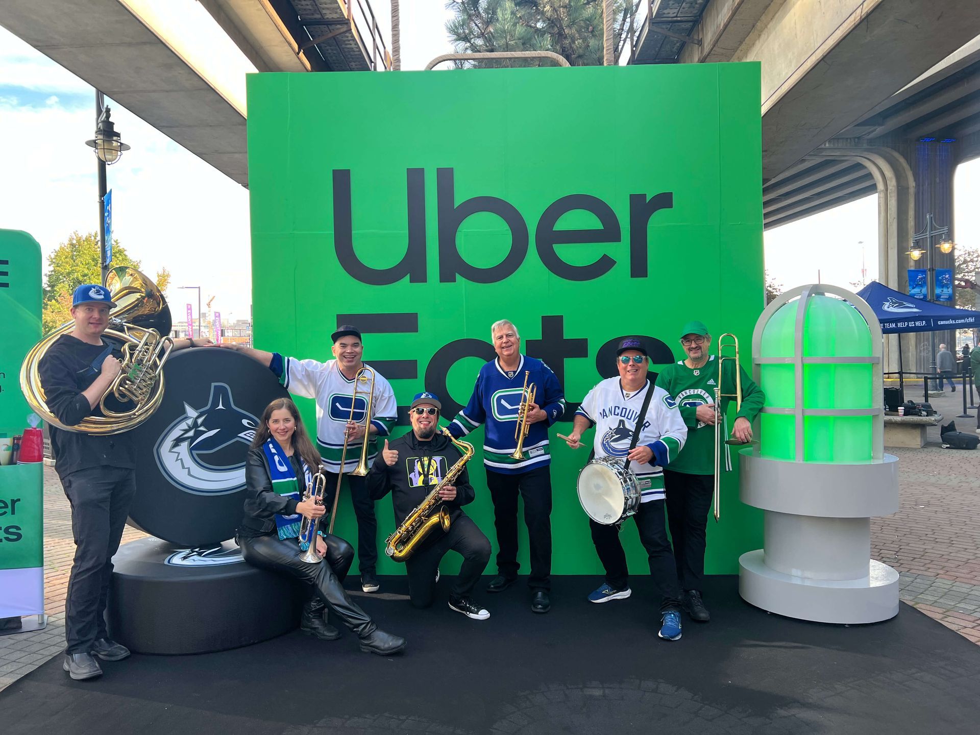 People posing at an Uber event booth with a bright green Uber backdrop and scooters under an overpass