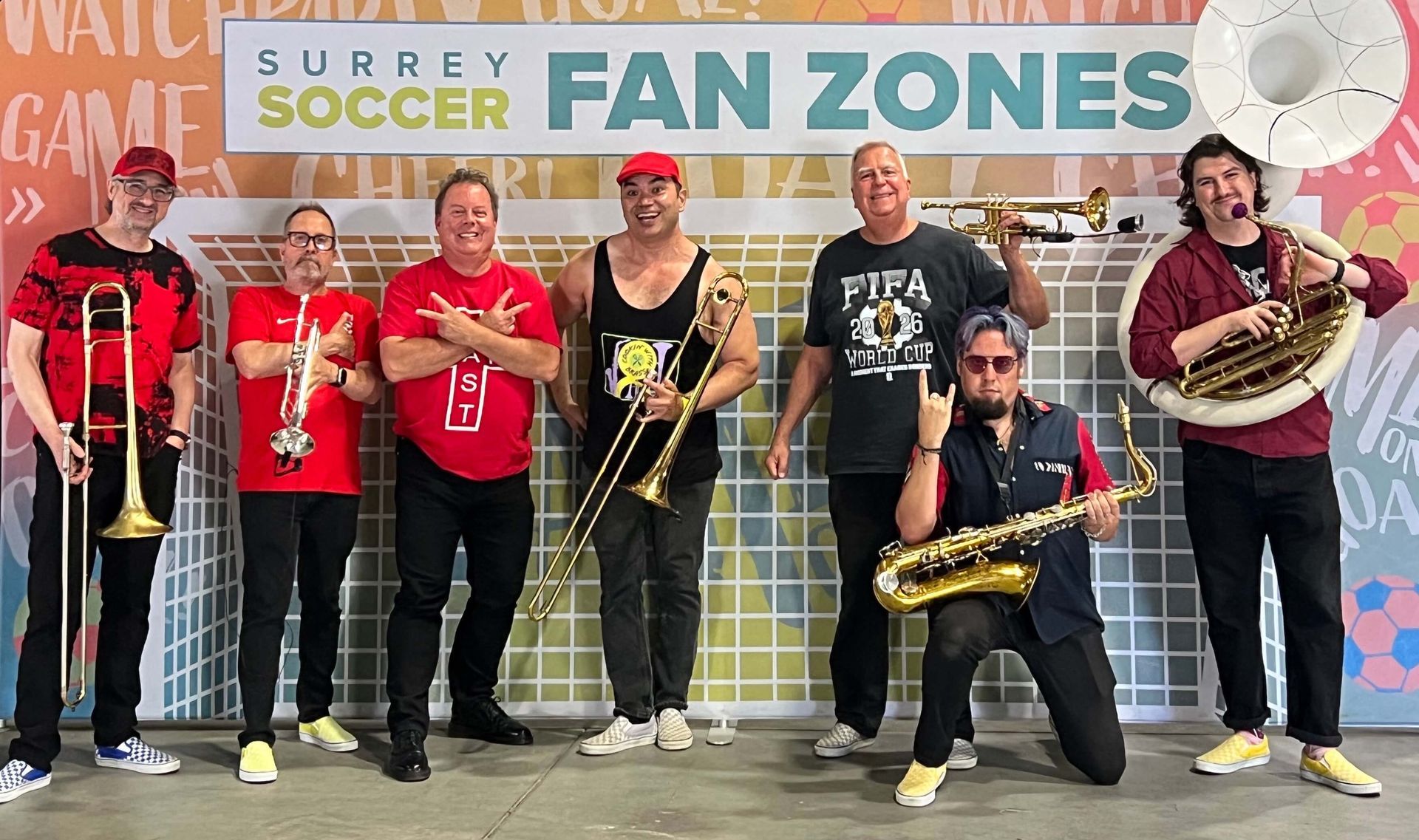 Band posing in front of Surrey Soccer Fan Zones mural, holding brass instruments and posing with a drum