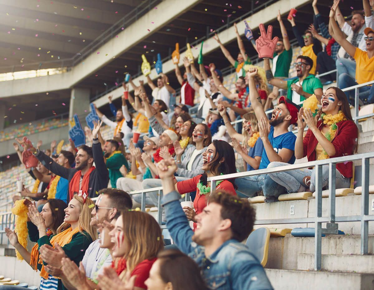 Cheering crowd in stadium stands, arms raised and clapping during a sports event
