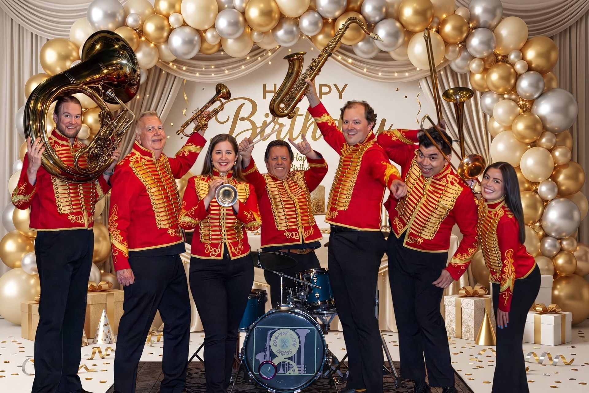 Band in red jackets performing onstage in front of gold balloons and a birthday backdrop